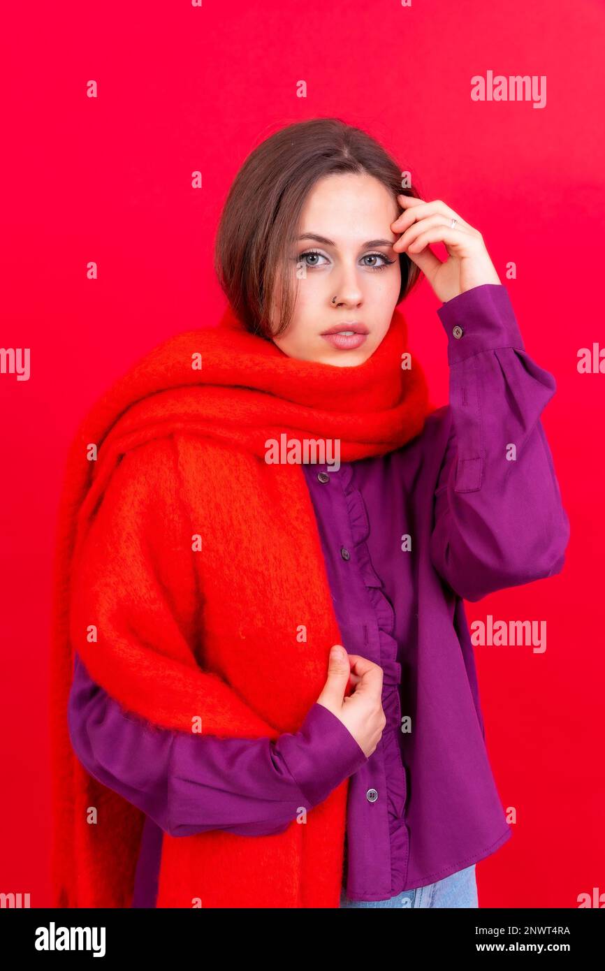 Close up portrait of a young caucasian woman in purple shirt isolated on red background, wearing a scarf looking at camera Stock Photo