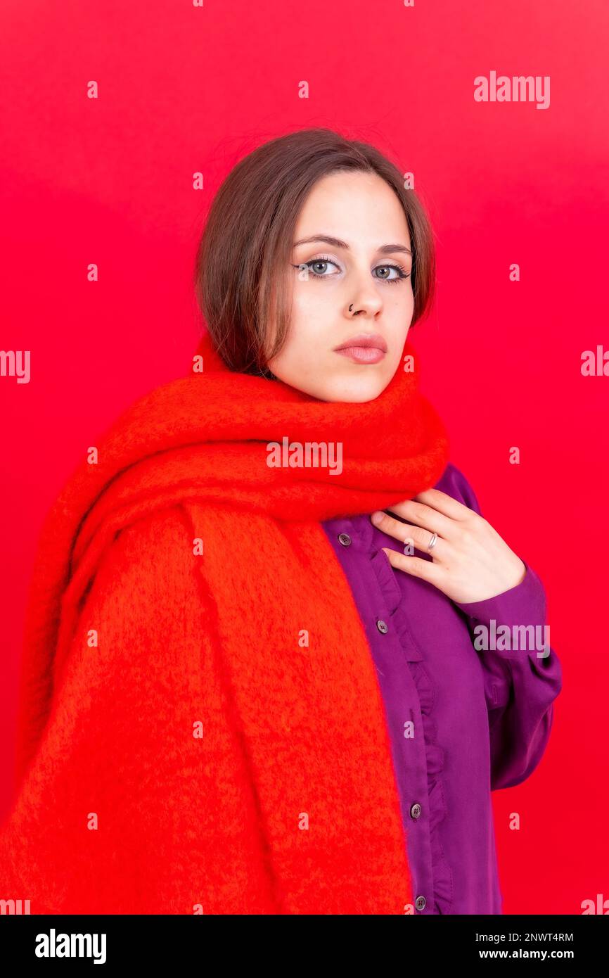 Close up portrait of a young caucasian woman in purple shirt isolated on red background, wearing a scarf Stock Photo