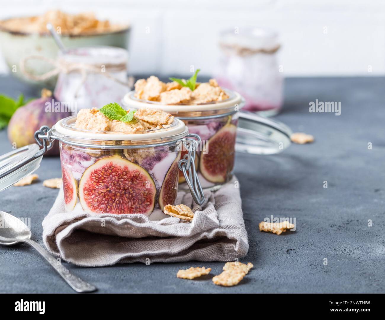 Homemade healthy yoghurt in glass pot with cereals, figs, mint on rustic concrete background