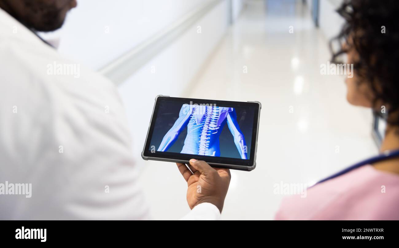 Diverse male and female doctors with stethoscopes using tablet with digital human in hospital. Health, hospital ward and care concept. Stock Photo