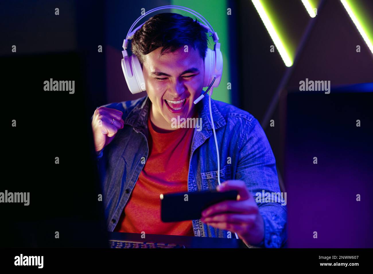 Male video game player cheering and celebrating as he streams a live broadcast of a game on his smartphone. Young man joining an online audience in wa Stock Photo