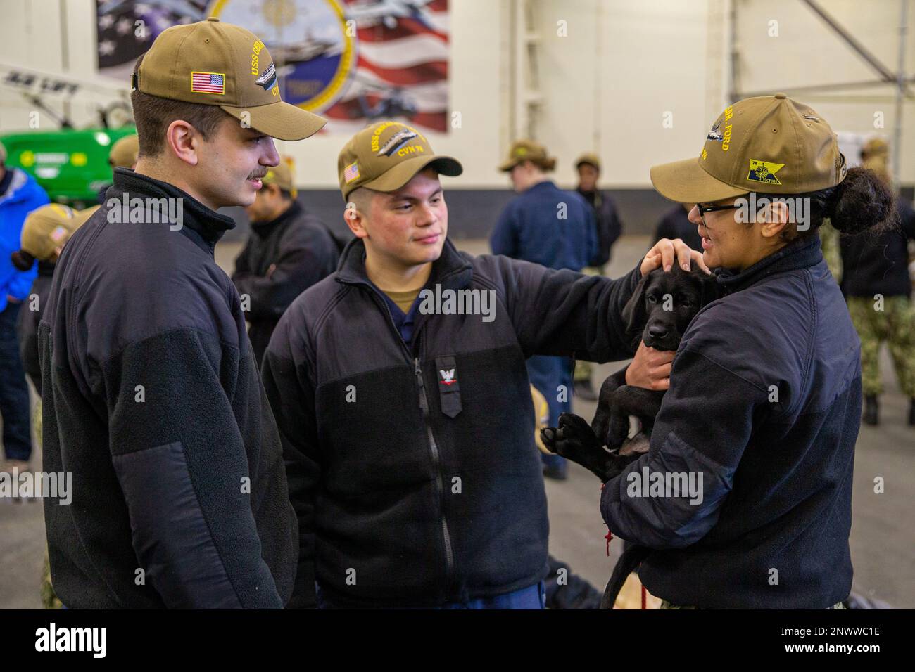 Retail Specialist Seaman Timothy Whiteside, left, from Valparaiso, Indiana, Retail Specialist 3rd Class Adriel Garcia-Castaneda, center, from Jonesboro, Georgia, and Retail Specialist 3rd Class Samantha Chacon, from El Paso, Texas, play with a dog, assigned to Mutts with a Mission, aboard the first-in-class aircraft carrier USS Gerald R. Ford (CVN 78), Feb. 1, 2023. Mutts with a Mission brought their puppies-in-training on board Ford as a morale-reinforcing opportunity by collaborating with the ship’s Morale, Welfare and Recreation department. Stock Photo