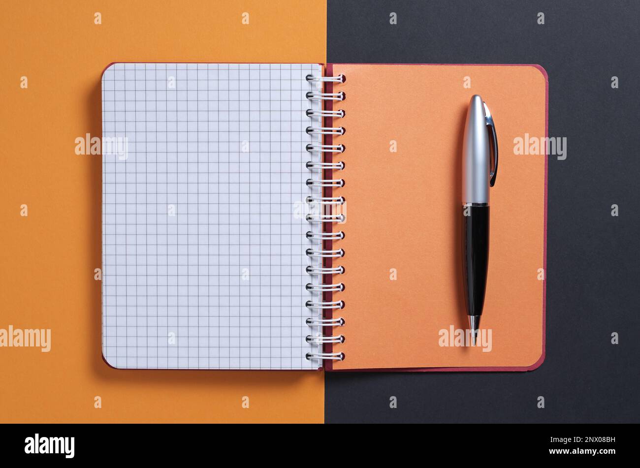 Notebook and pen on black-orange background, top view Stock Photo