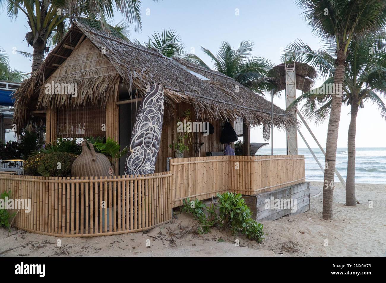 Beach bungalow made of palm leaves on the beach with a surfboard Stock Photo
