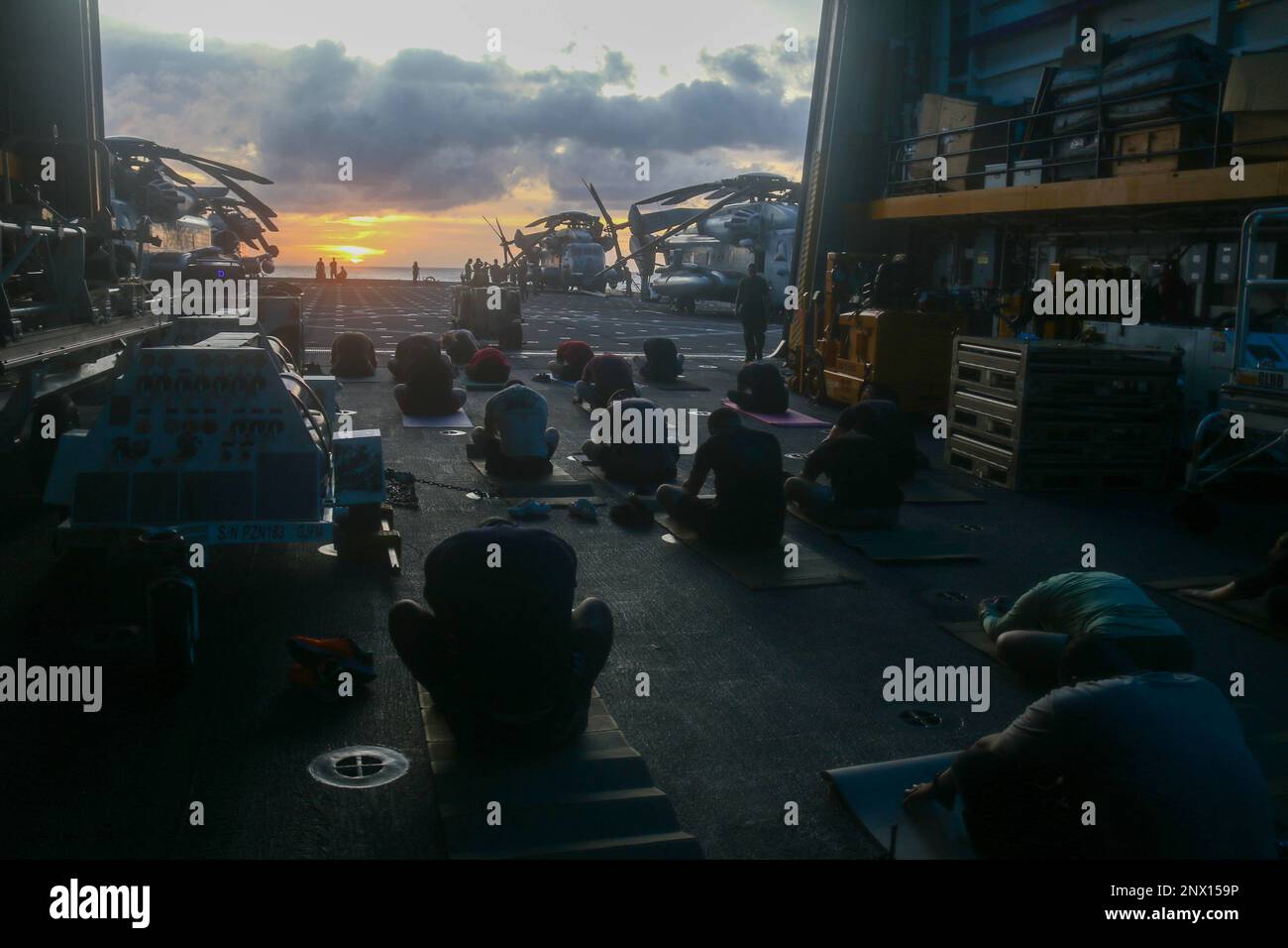 SOUTH CHINA SEA (Feb. 4, 2023) - Sailors, and Marines with the 13th Marine Expeditionary Unit, participate in a yoga class during sunset aboard amphibious transport dock ship USS John P. Murtha (LPD 26), Feb. 4 2023. Fitness is an integral part of the life of Sailors and Marines onboard, producing and strengthening a more competitive and lethal force. The Makin Island Amphibious Ready Group, comprised of amphibious assault ship USS Makin Island (LHD 8) and amphibious transport docks USS Anchorage (LPD 23) and USS John P. Murtha (LPD 26), is operating in the U.S. 7th Fleet area of operations wi Stock Photo