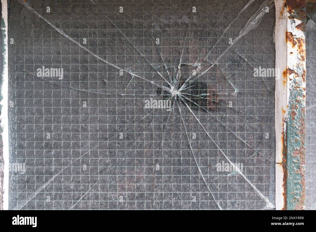 Cracks radiate from a central impact point on a reinforced window. Stock Photo