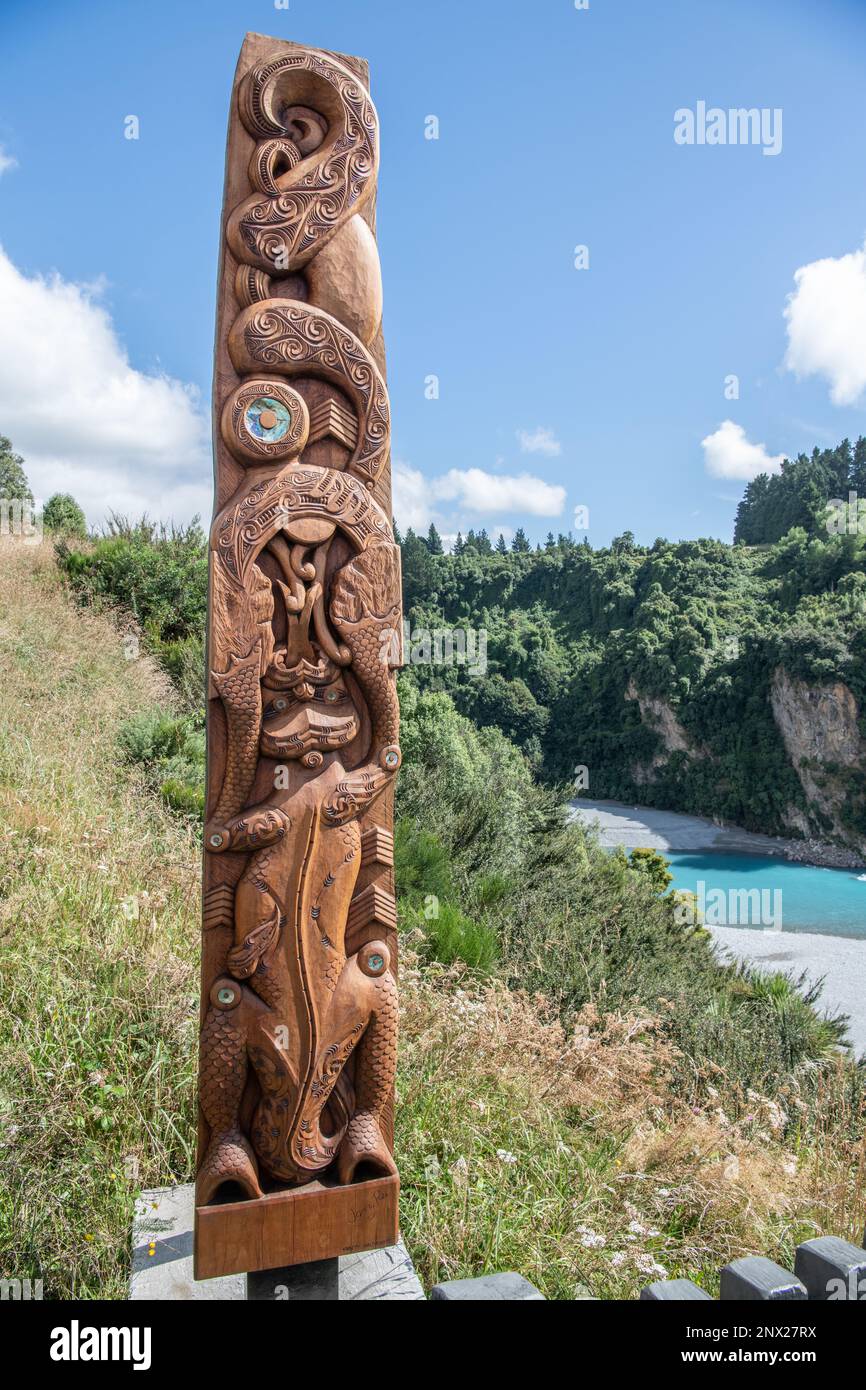 A wooden pou carving of a Taniwha from Maori mythology next to the Rakaia River and Gorge in Aotearoa New Zealand. Stock Photo