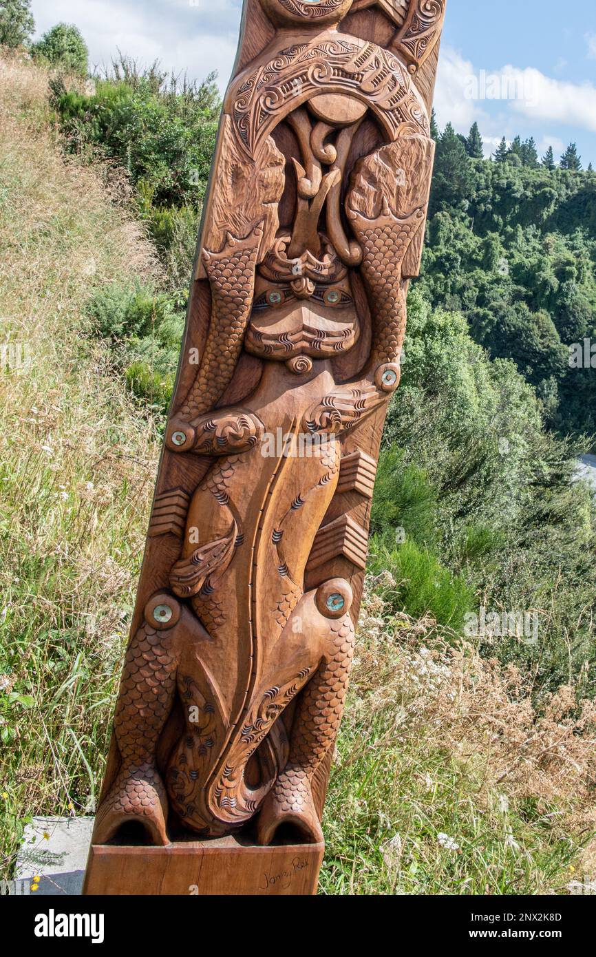 A wooden pou carving of a Taniwha from Maori mythology next to the Rakaia River and Gorge in Aotearoa New Zealand. Stock Photo