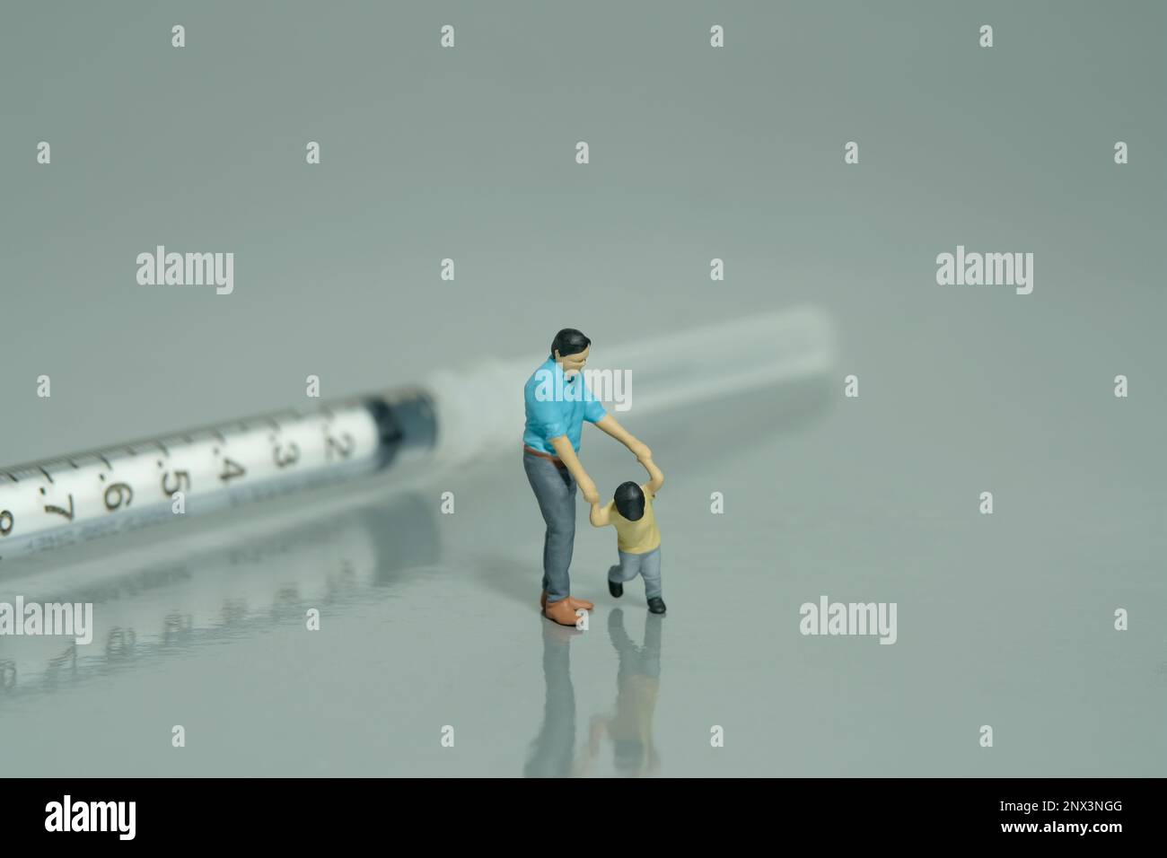 Miniature people toy figure photography. Refusing for injection concept. A father and son standing in front of needle syringe on grey background. Imag Stock Photo