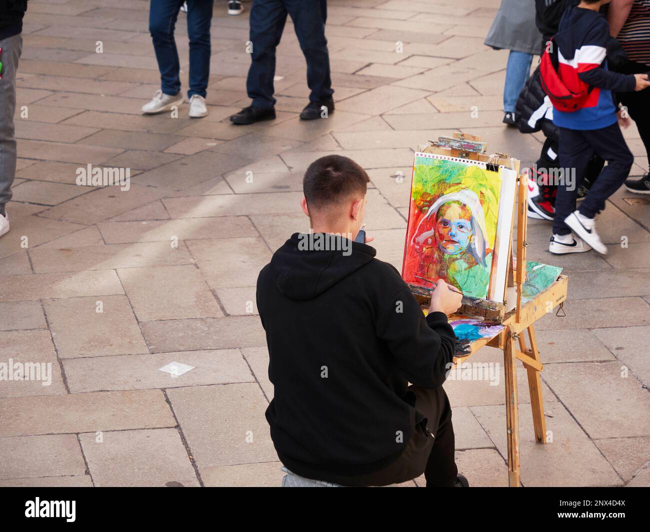 A young street portrait painter waiting for his next customer in Venice Italy with people walking by. Stock Photo