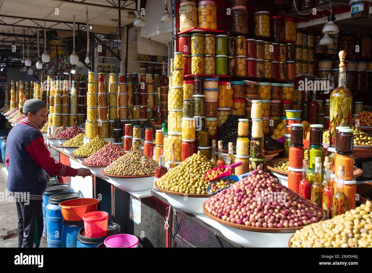 Marrakech, Morocco – February 25, 2023: A man is cleaning his counter with olive and pickled vegetables and fruit in glass jars Stock Photo