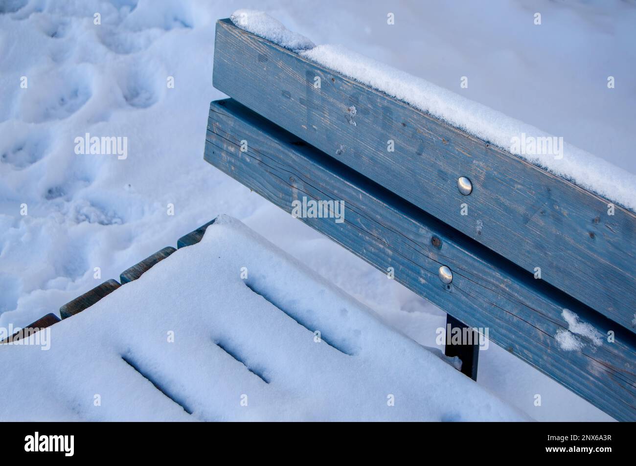 Light blue wooden bench covered by snow in a public park in Finland ...