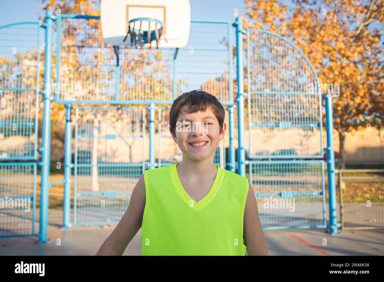 Half-length portrait of a smiling boy in a tank top smiling at the camera on an urban basketball court at dusk. Stock Photo