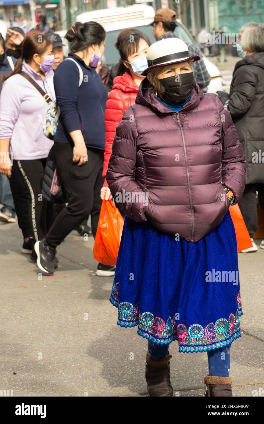A South American woman wearing traditional skirt & hat and a mask walks on Main St in Chinatown, Flushing, Queens, New York City. Stock Photo