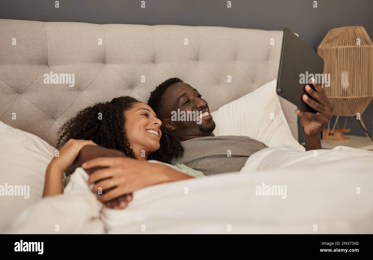 Smiling multiracial couple using a tablet in their bed Stock Photo