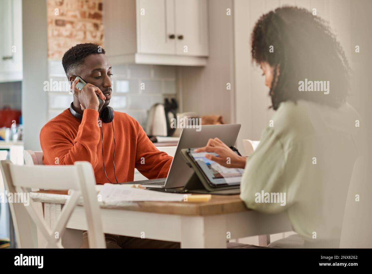 Young multiracial couple working online remotely at their kitchen Stock Photo