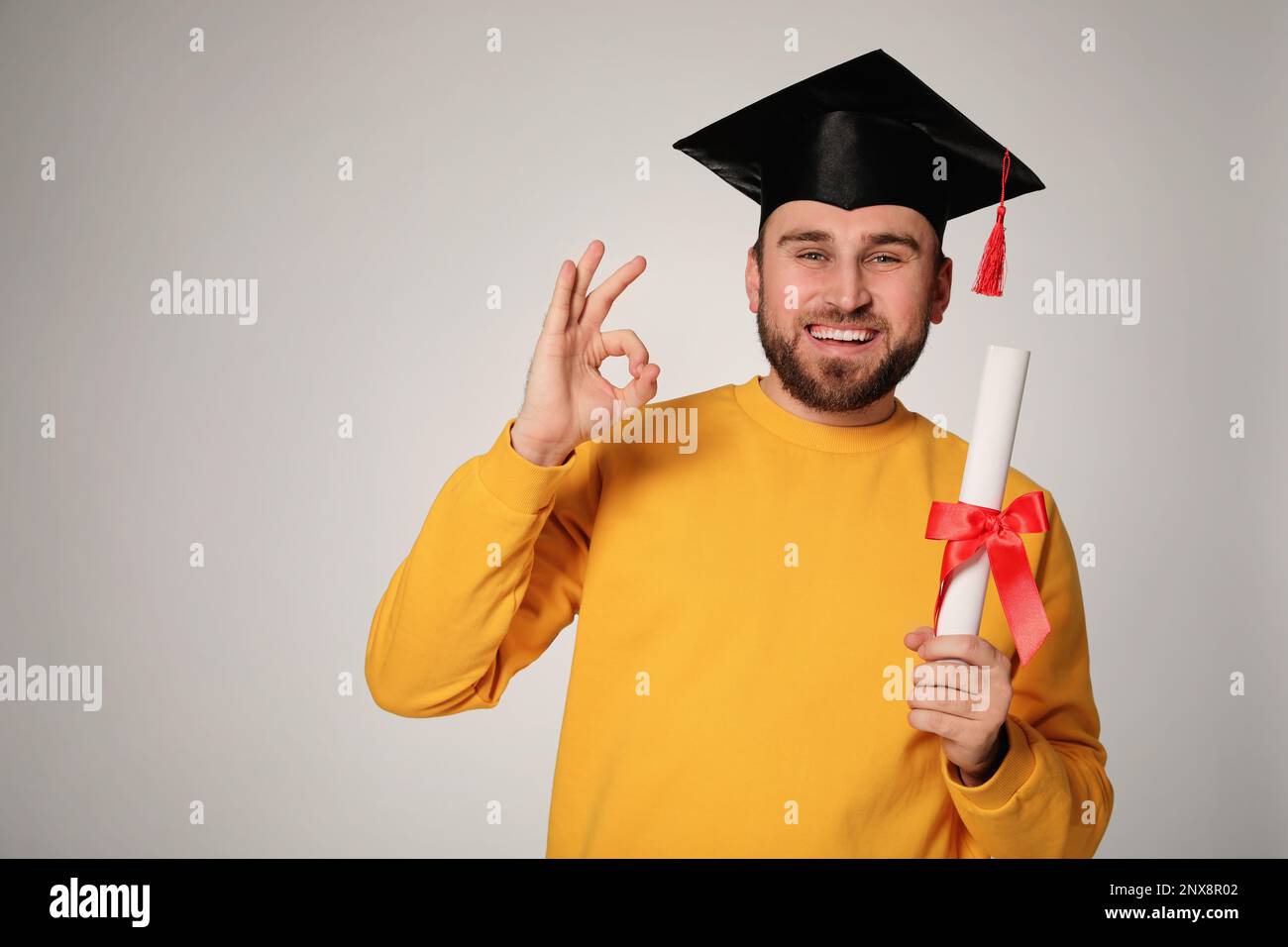 Happy student with graduation hat and diploma on grey background. Space ...