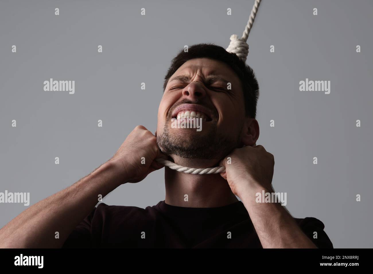 Depressed man with rope noose on neck against light grey background Stock Photo