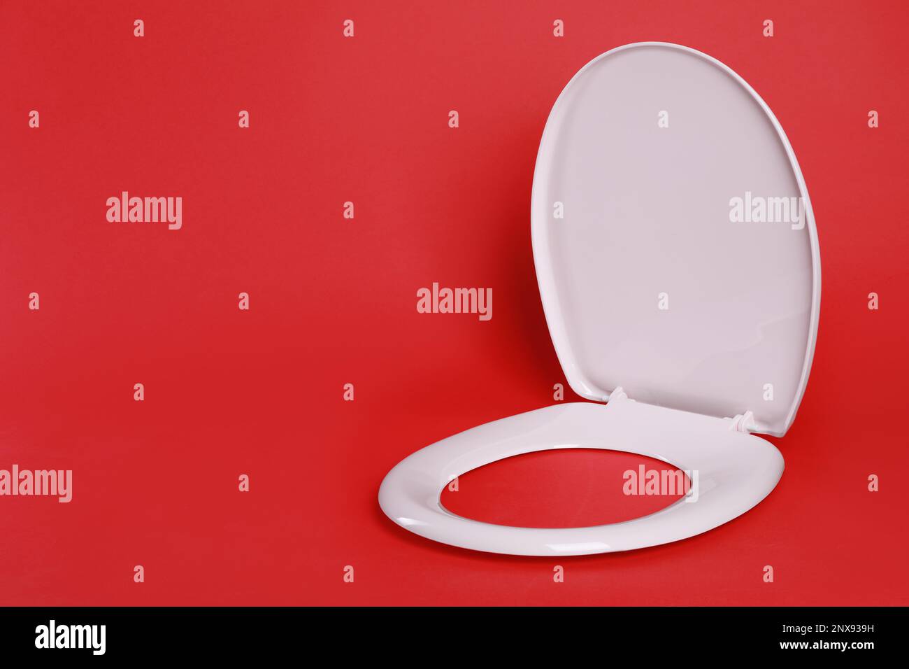 New pink plastic toilet seat on red background, space for text Stock Photo