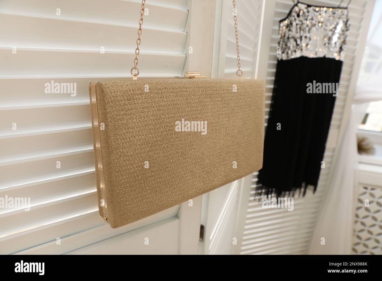 Stylish bag and dress hanging on white folding screen, closeup