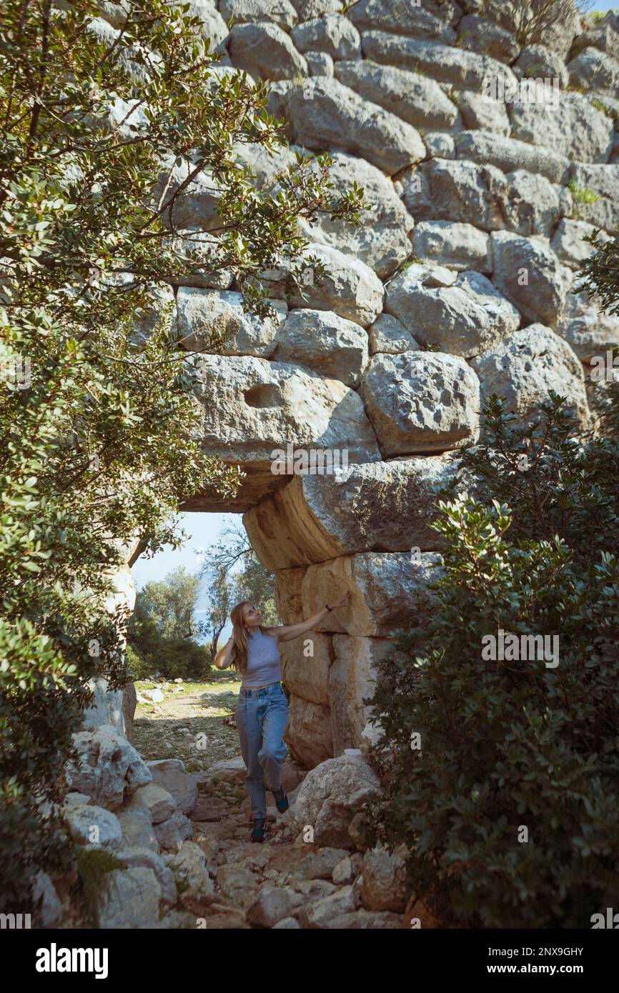 Young woman look at ruins of old Roman Delikkemer aqueduct bridge at Lycian way. Patara Ancient City at location Kalkan, Kas, Antalya. Popular travel Stock Photo