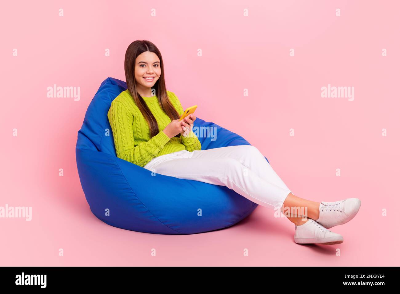 Full size photo of lovely teen lady sitting blue bean bag hold device