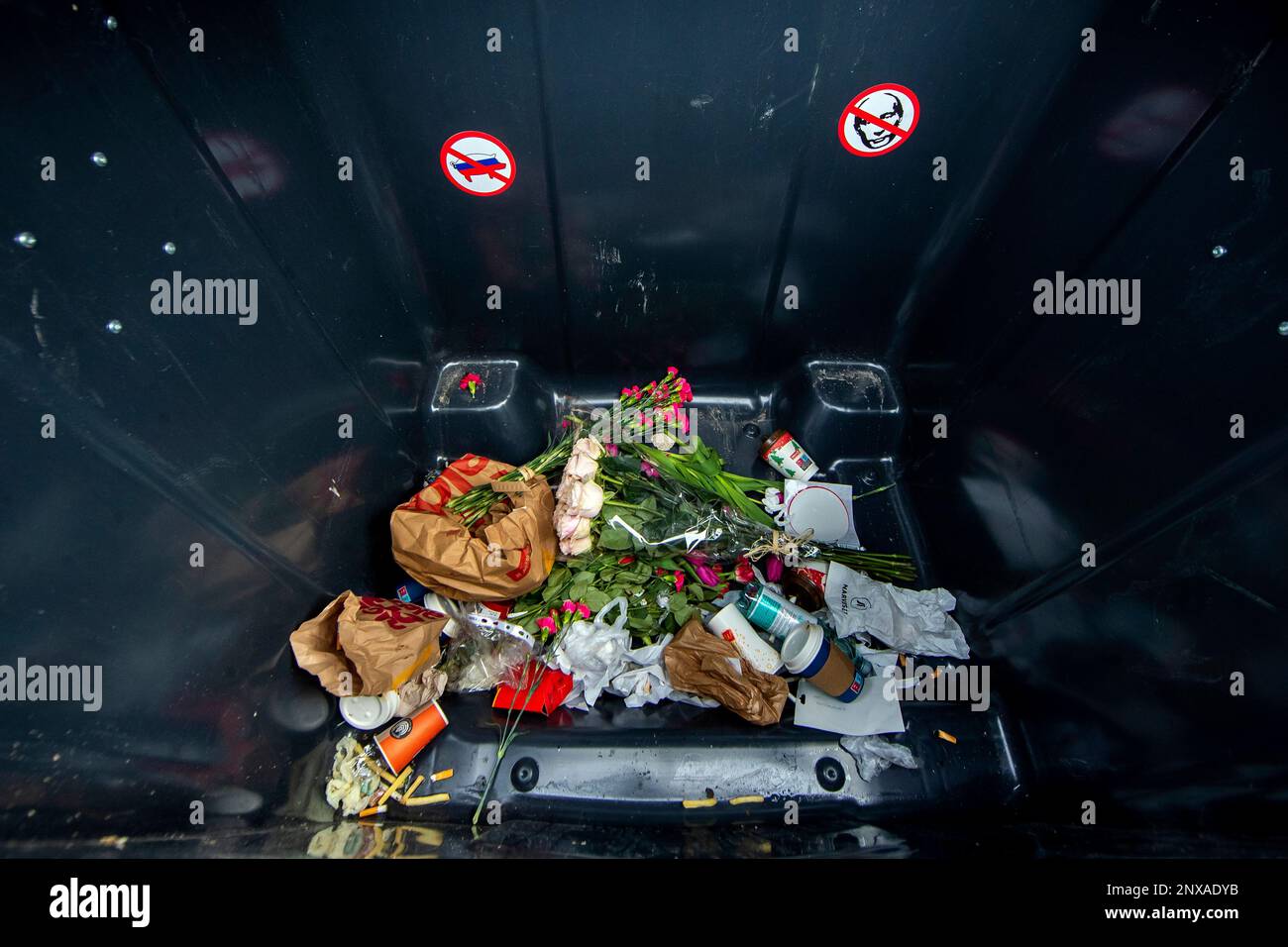 Flowers are seen amongst other garbage inside a garbage container which ...