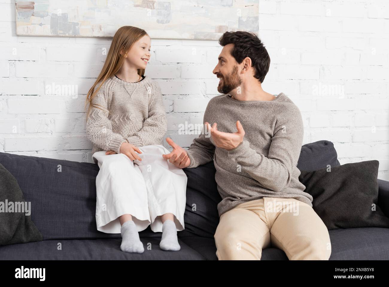 bearded man gesturing while talking to smiling daughter on couch in living room,stock image Stock Photo
