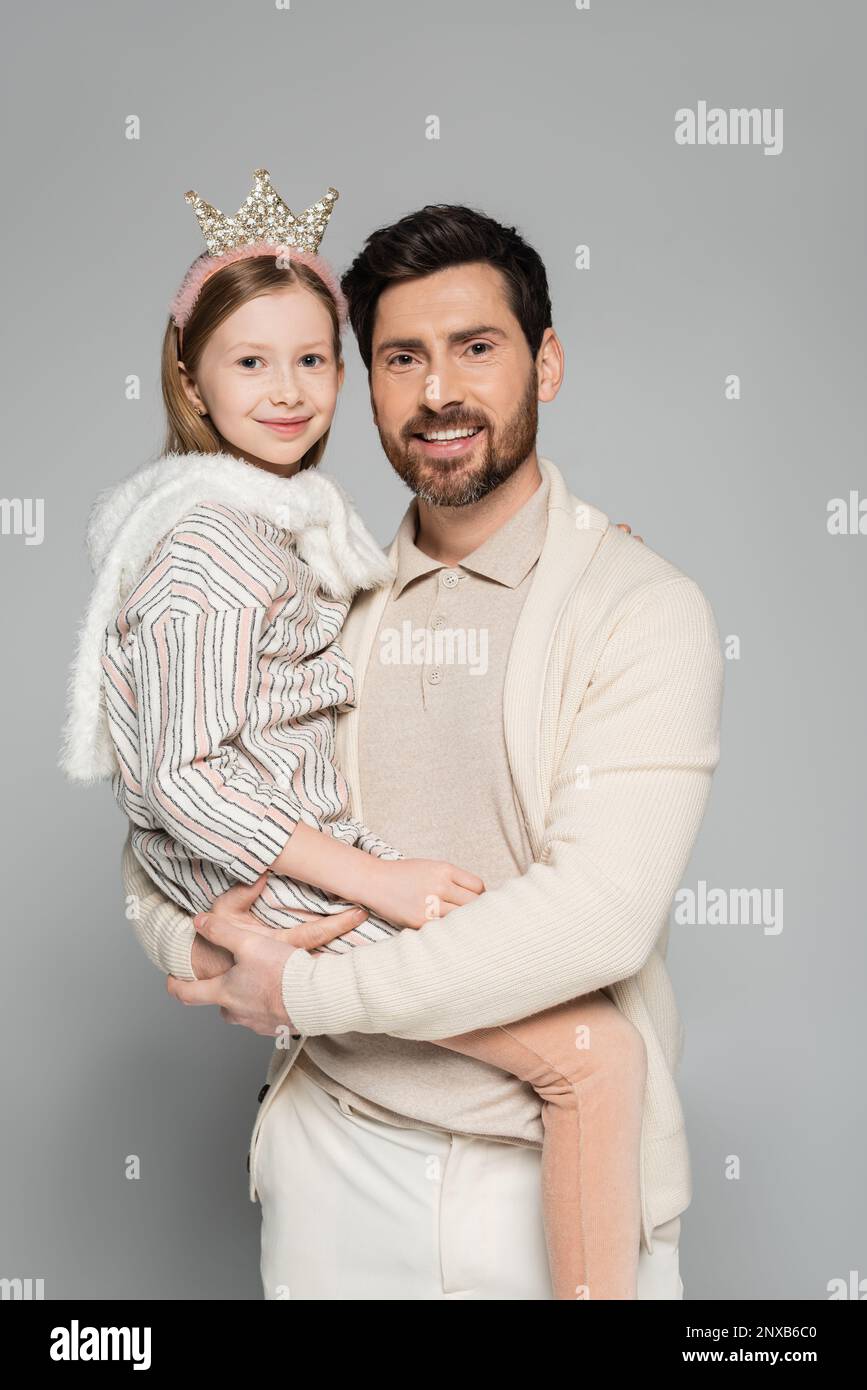 happy father lifting cheerful daughter in crown and dress isolated on