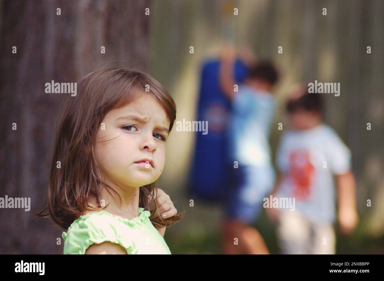 Portrait of an unhappy girl feeling left out with two boys playing in the background, USA Stock Photo