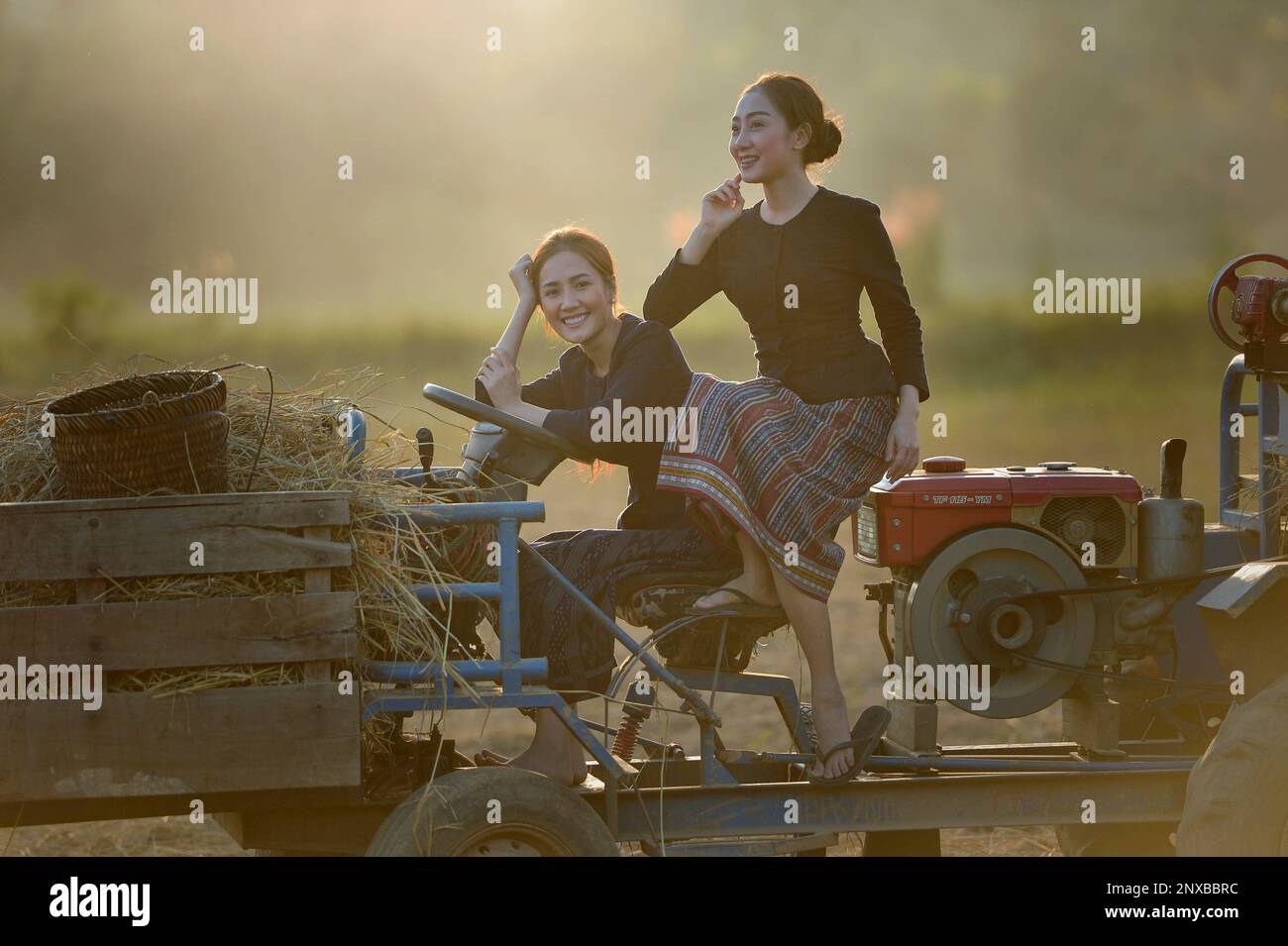 Two smiling women sitting on a tractor in a field, Laos Stock Photo