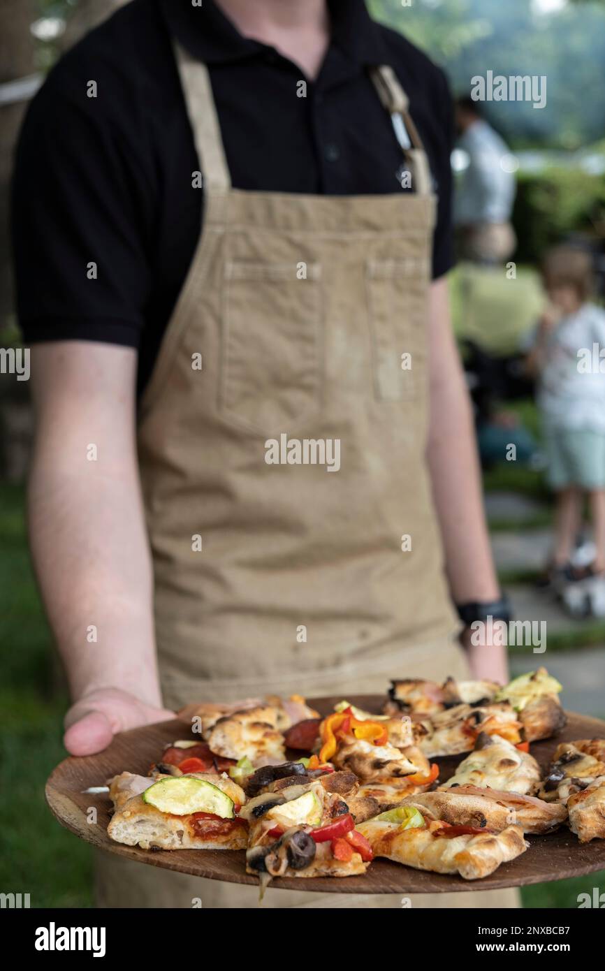 Closeup of a person offering slices of pizza in a garden Stock Photo