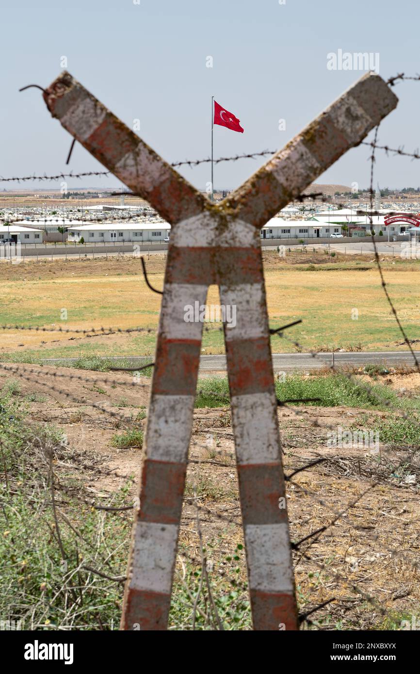 Turkish Flag  and Elbeyli Temporary Accommodation Center visible behind barbed wire in selective focus. Barbed wire and concrete pole is out of focus. Stock Photo