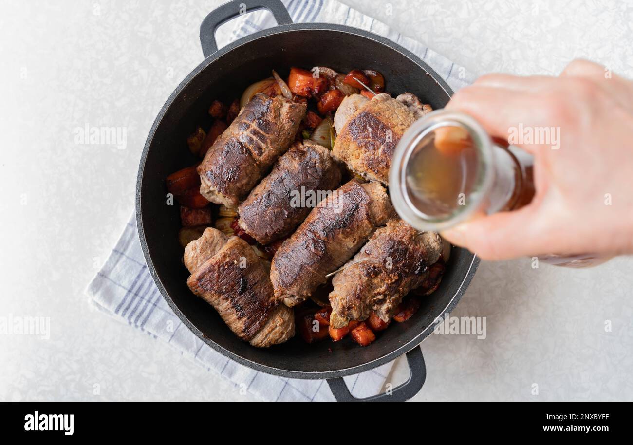 Pouring beef broth into a roasting pan with beef roulades and roasted