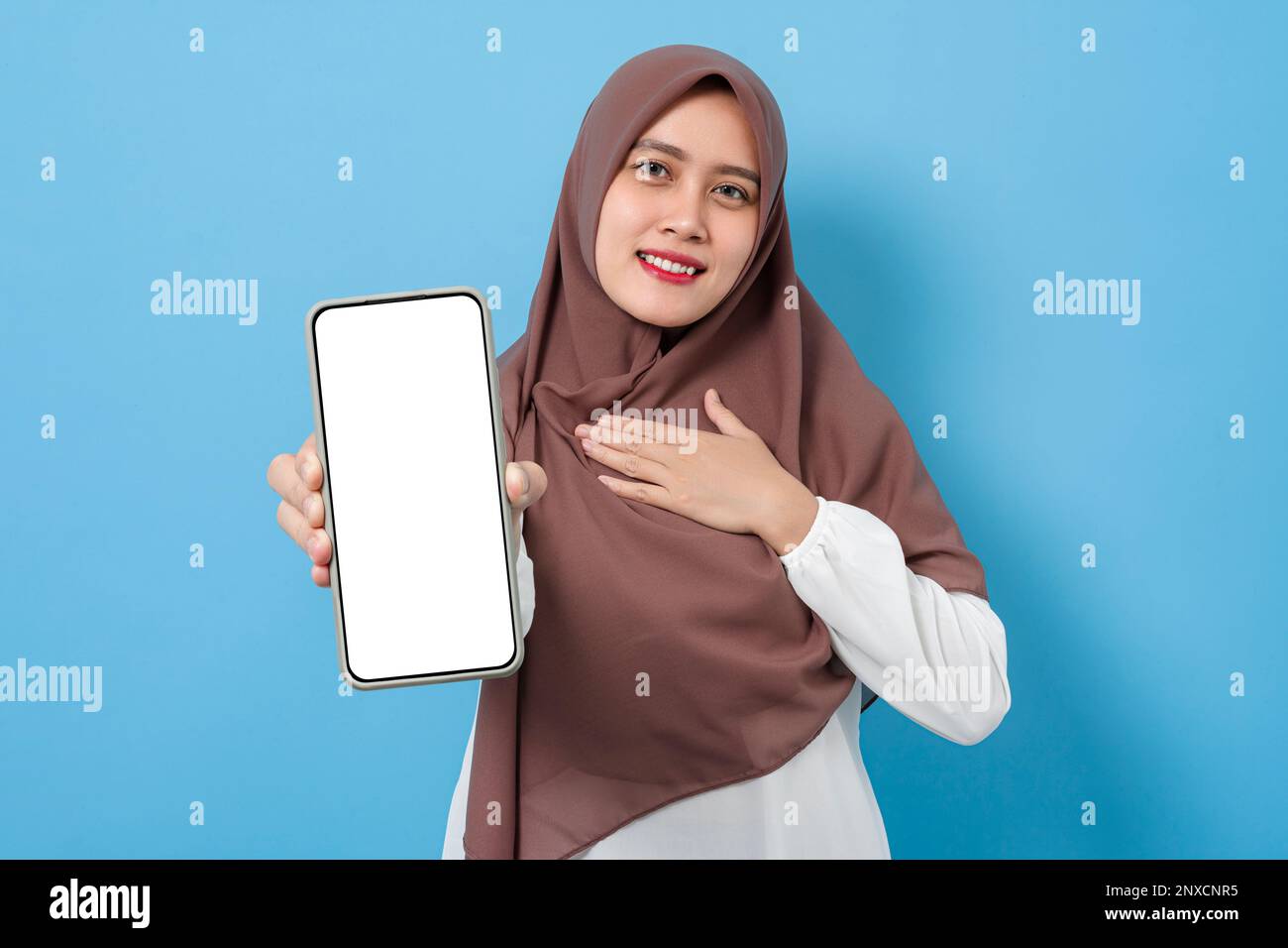 Happy smiling muslim woman showing blank smartphone screen for mock up isolated on blue