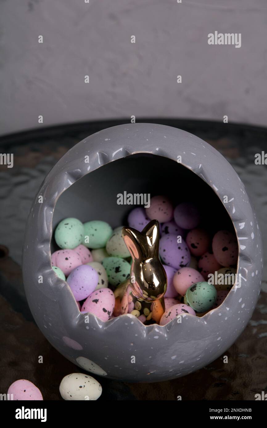 photo a lot of colored Styrofoam eggs lying in a large gray egg and inside is a rabbit on a glass table Stock Photo