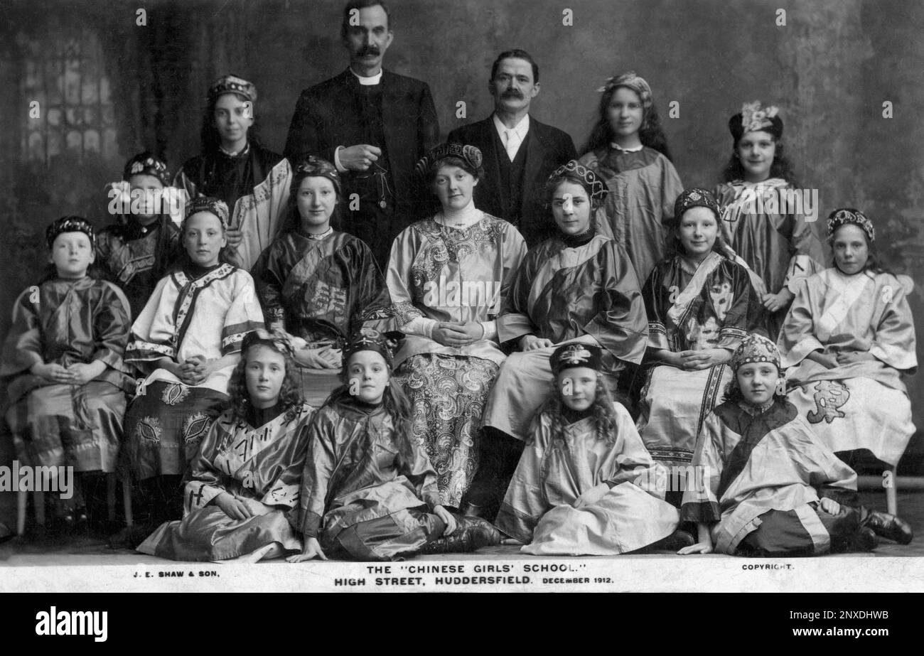 The Far East comes to West Yorkshire, England, UK: girl pupils of the ‘Chinese Girls’ School’ in Huddersfield High Street sit in December 1912 for a group portrait with their teachers and a clergyman while exotically dressed in Chinese costume typical of the era.  Monochrome vintage postcard published by Huddersfield and Sheffield photographers, John Edward Shaw & Son. Stock Photo