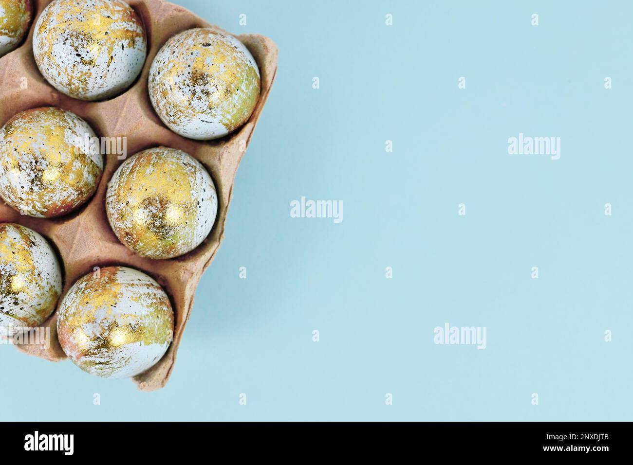 Painted Easter eggs with golden spots in egg carton on blue background