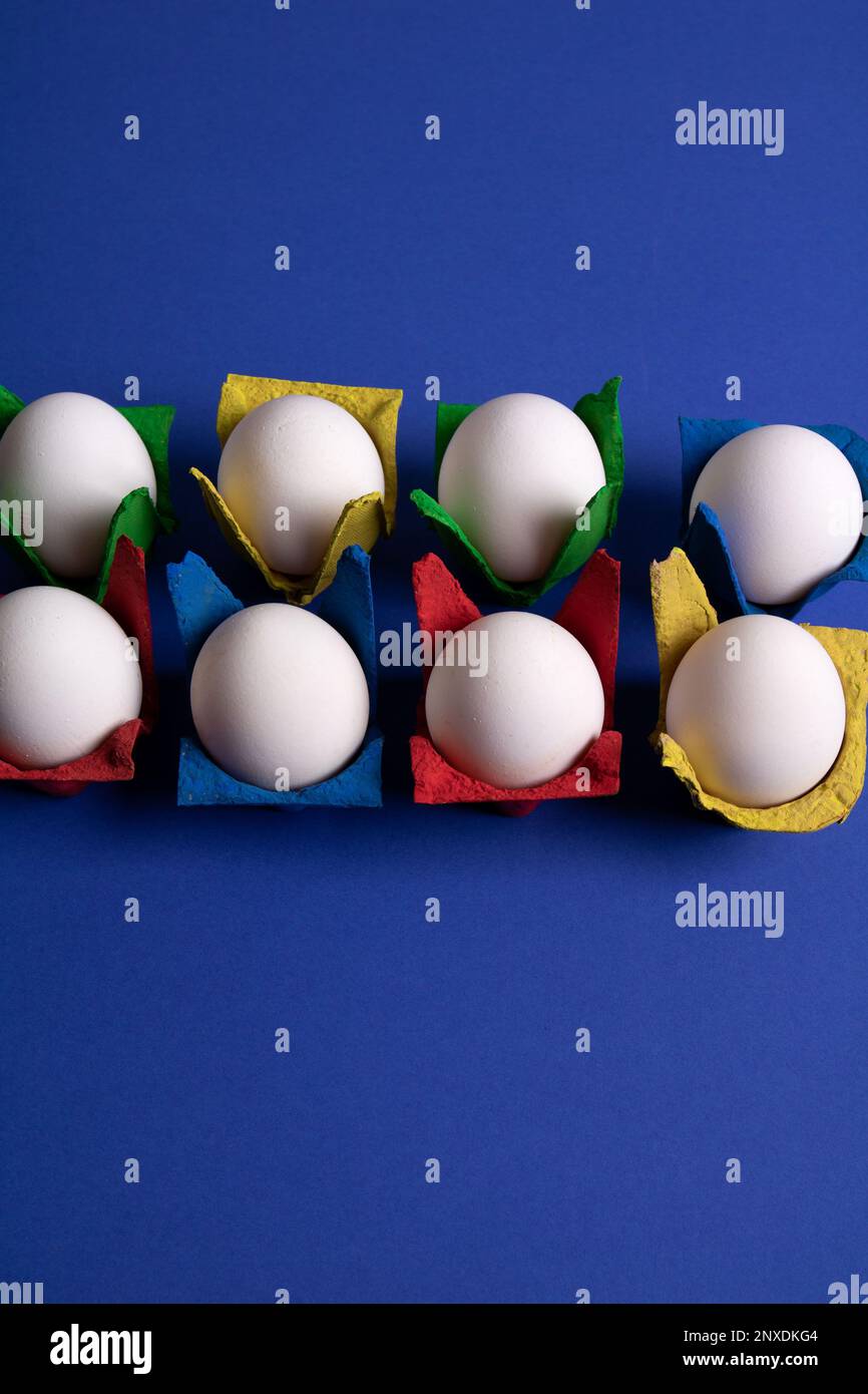 photo eight white hen eggs in colored packages on a blue background Stock Photo