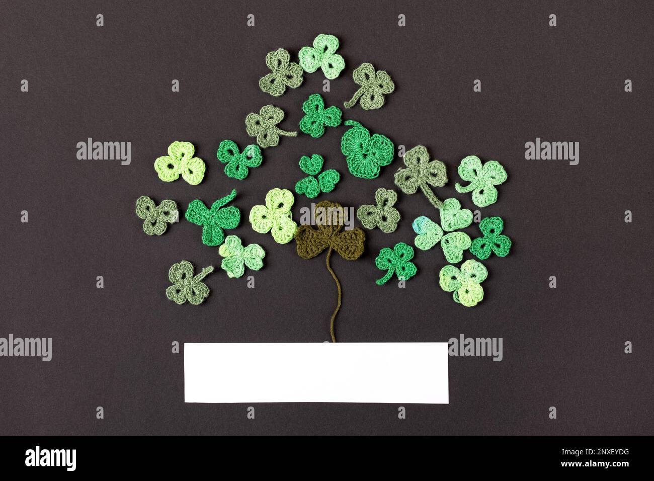 St Patrick's Day concept. Composition made of knitted green shamrocks in the form of three-leaf clover on a black background. Holiday sign and knitted Stock Photo