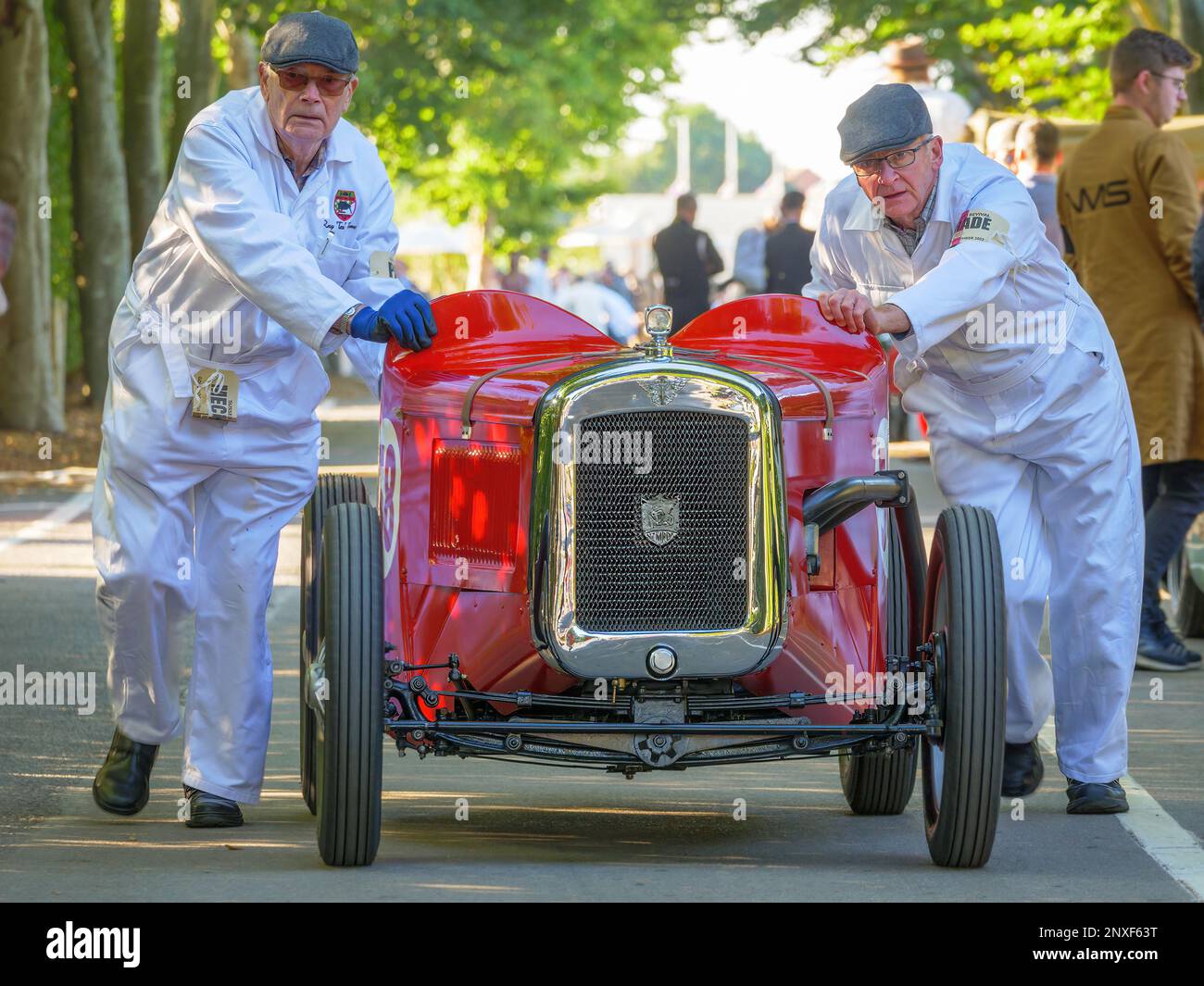 Two mechanics pushing a red Austin 7 racing car at the Goodwood Revival 2022, West Sussex, uk Stock Photo