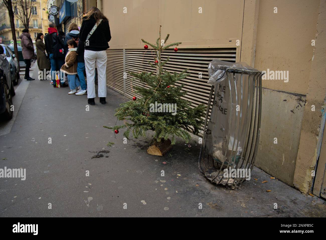 Christmas tree left next to a garbage can near a popular restaurant with a queue in the street Stock Photo