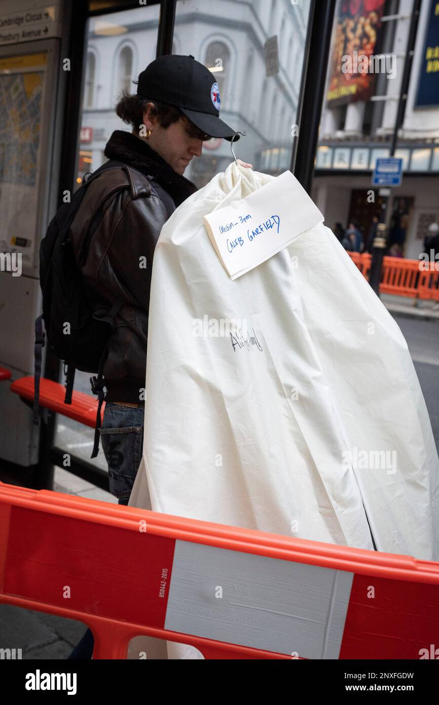 A man holding a covered item of clothing stands at a bus stop in the capital's West End, on 28th February 2023, in London, England. Stock Photo