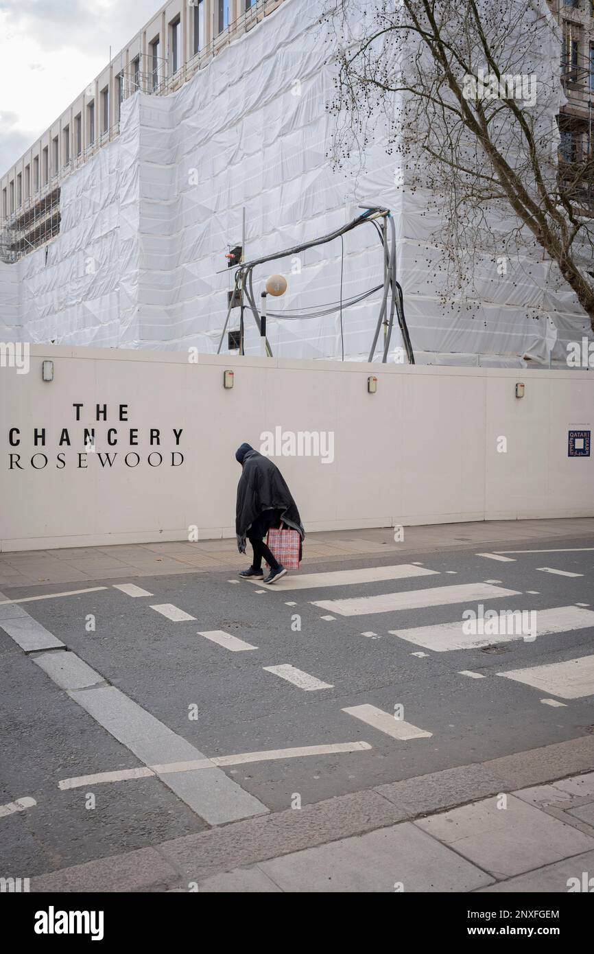 With the former US Embassy being refevloped into a luxury property in the background, a woman who is bent over crosses the road on a zebra crossing in Grosvenor Square in Mayfair, on 27th February 2023, in London, England. The Chancery Rosewood, in partnership with real estate developer Qatari Diar, is to open in 2024 at the location of the Grade II listed former U.S. Embassy building. Stock Photo