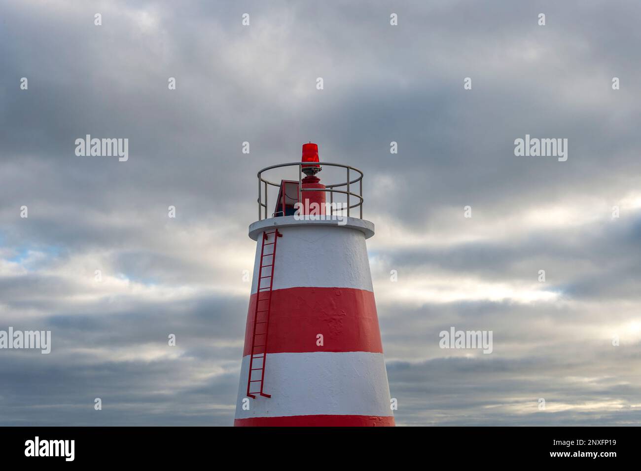 Top of a red and white lighthouse beacon against a cloudy sky. Stock Photo