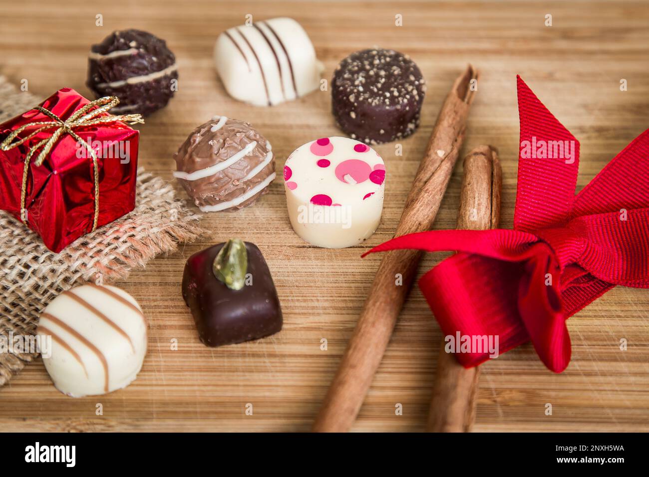 Chocolate pralines sweet Christmas candy. Small Packages with holiday decoration, red ribbon on wood. Stock Photo