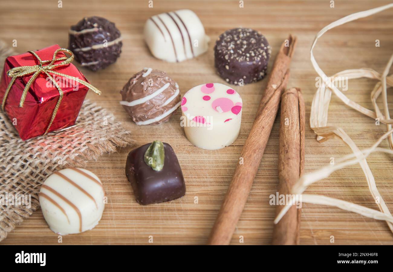 Variety of chocolate pralines, gift and truffles. Pralines with pink dots. Small red package and decorated with cinnamon stick. Stock Photo