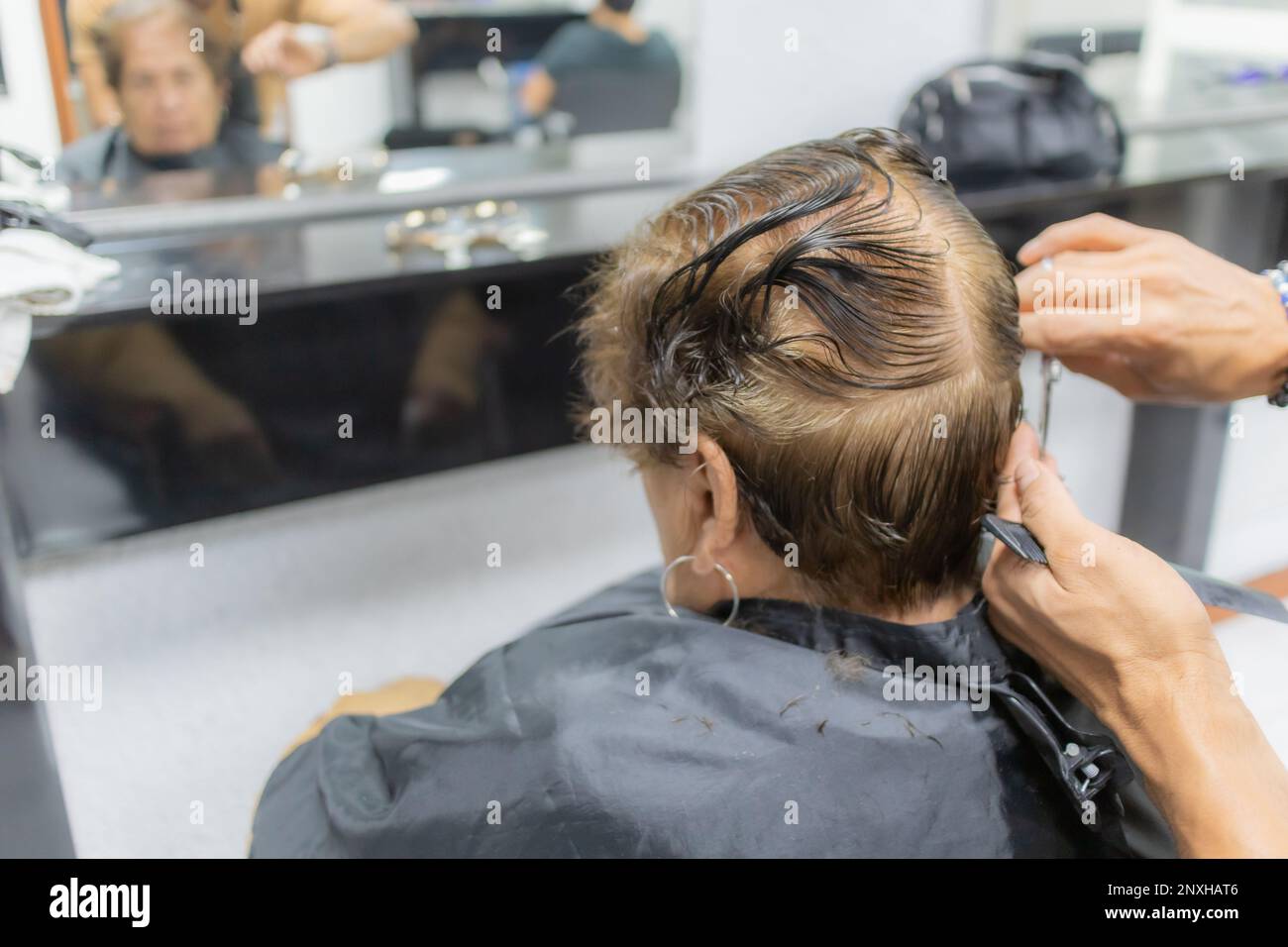 Hairdresser cutting the hair of an elderly woman, reflected in the