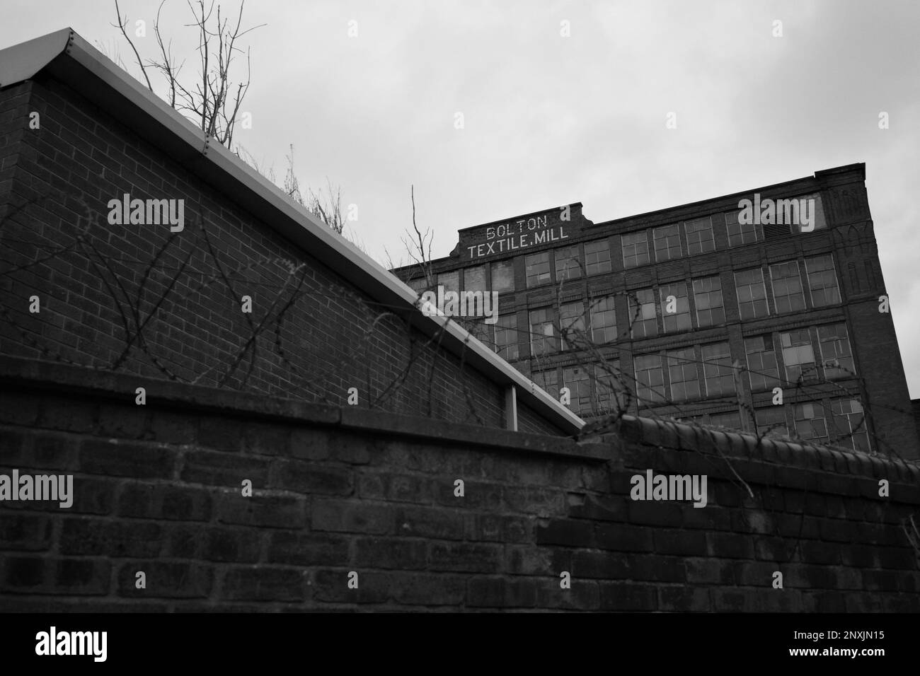 Bolton Textile Mill (Cawdor Street, Farnworth). A large brick building and a wall with barbed wire stands in front of the viewer. England, UK Stock Photo