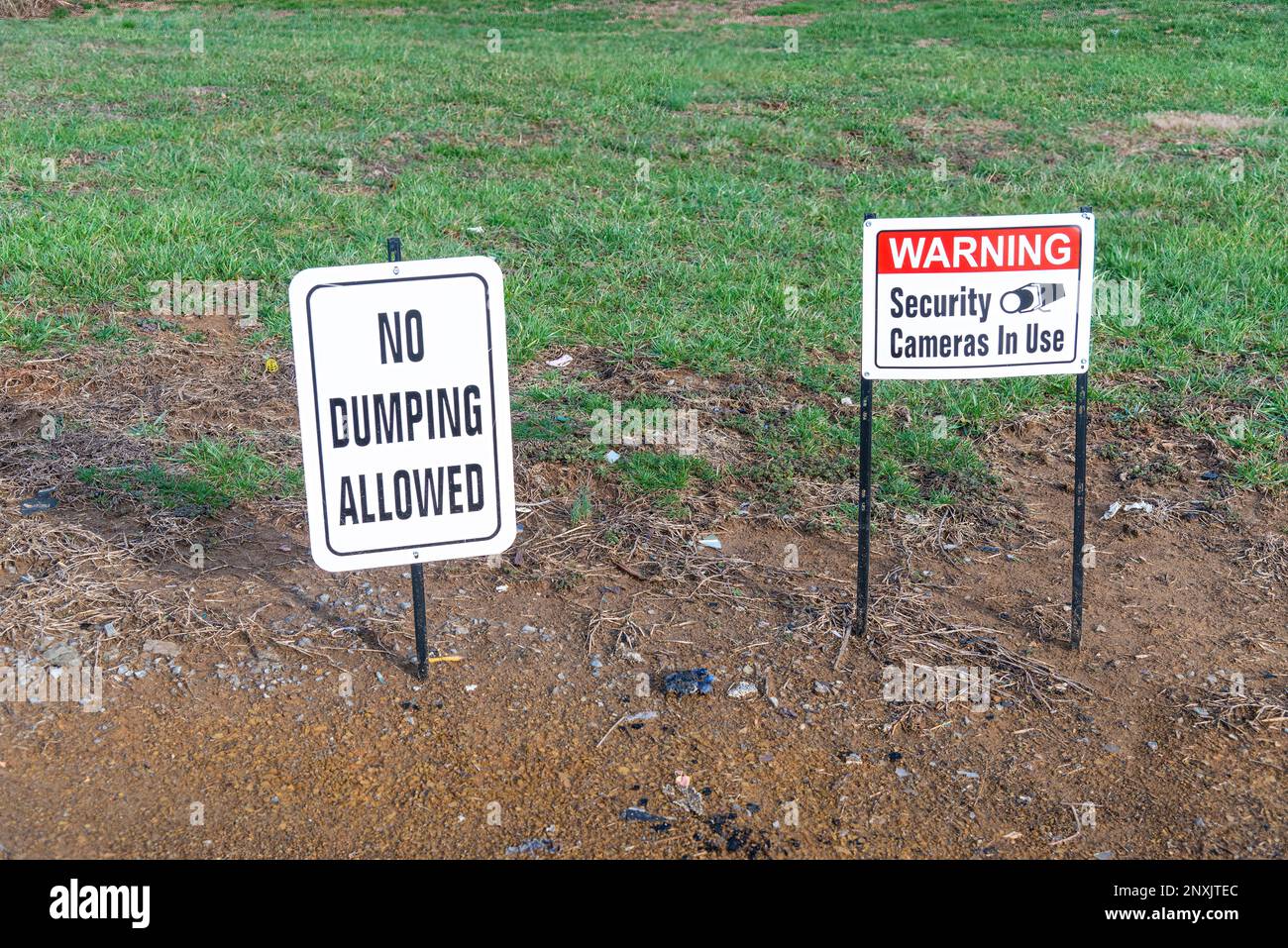 Horizontal shot of a No Dumping Allowed sign and a Warning Security Cameras In Use sign in a field. Stock Photo